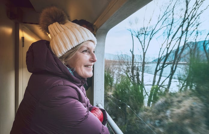 Women wearing a woolly hat and puffer jacket on a train looking out at the winter view