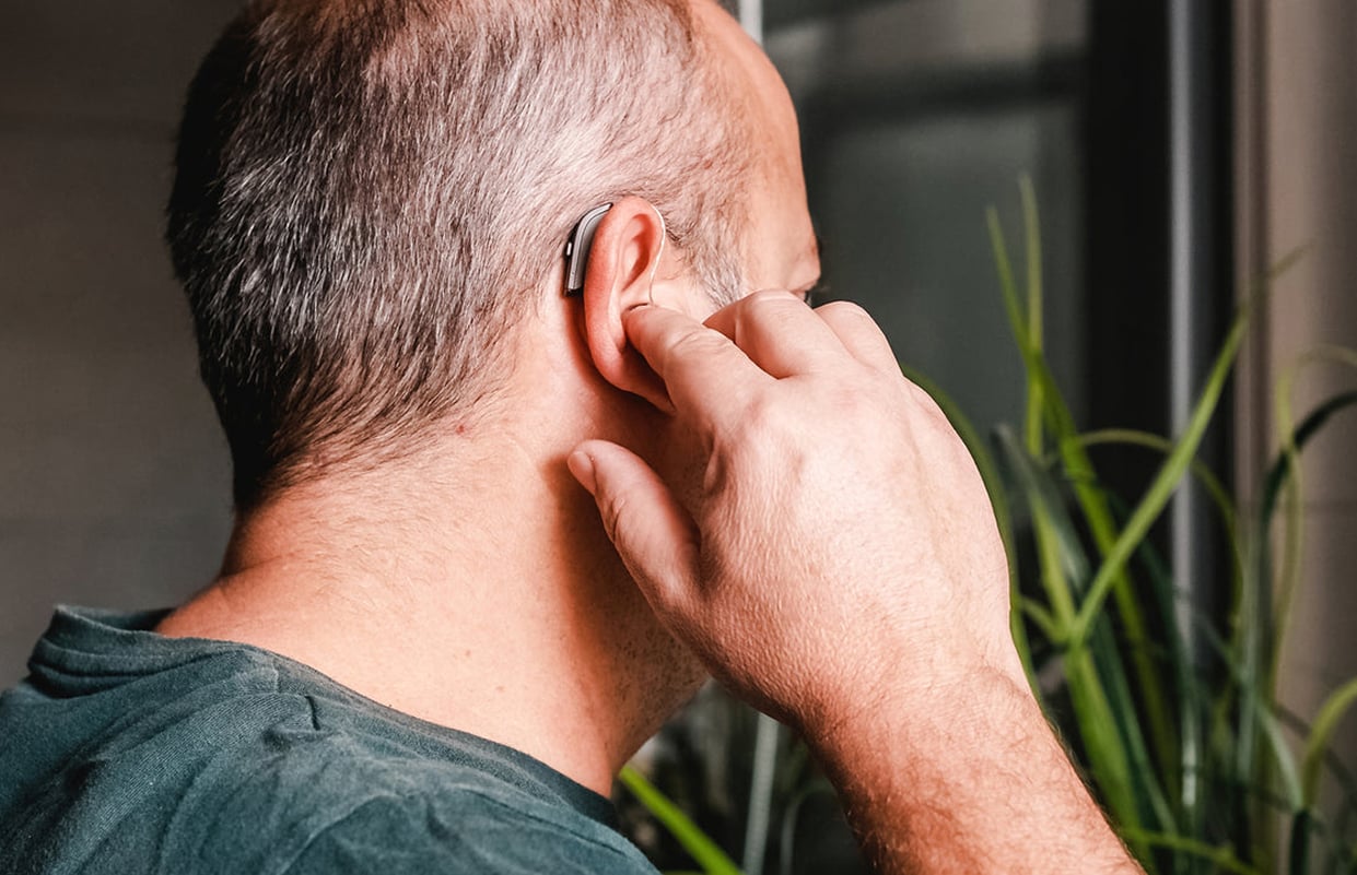 Middle-aged man adjusting a hearing aid at home